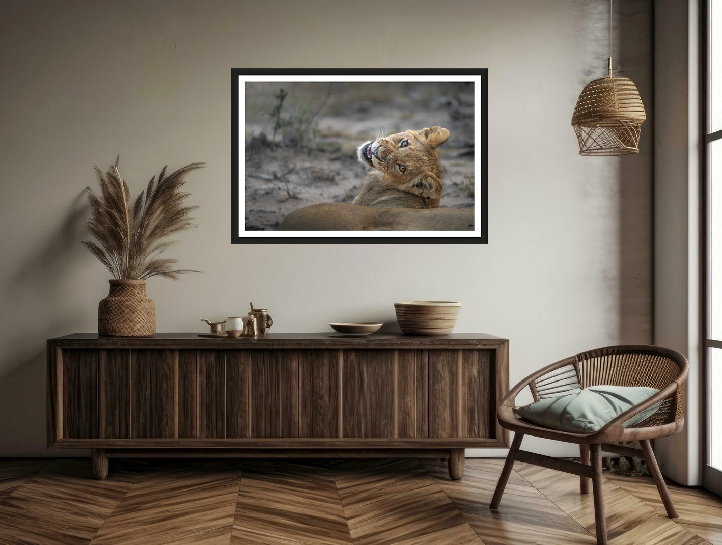 A photograph of a cute lion cub looking back over its shoulder into the camera smiling hanging on a brown wall above a commode and chair.