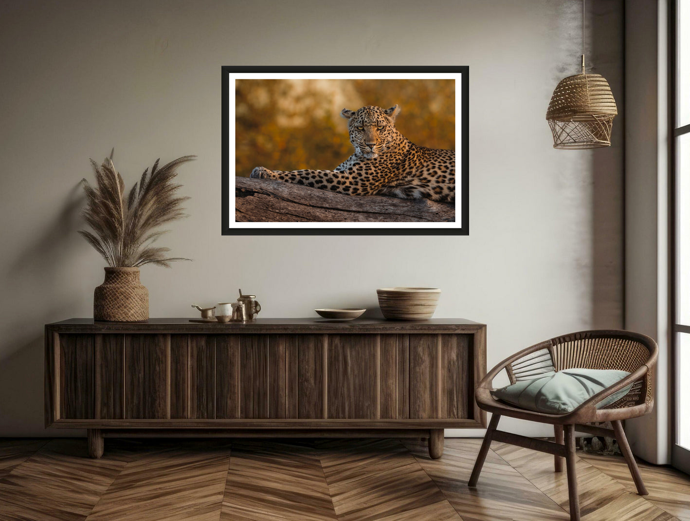 A photograph shwoing a closeup of a leopard laying on a branch with golden bokeh in the background while looking in to the camera hanging on a brown wall above a commode and a chair.