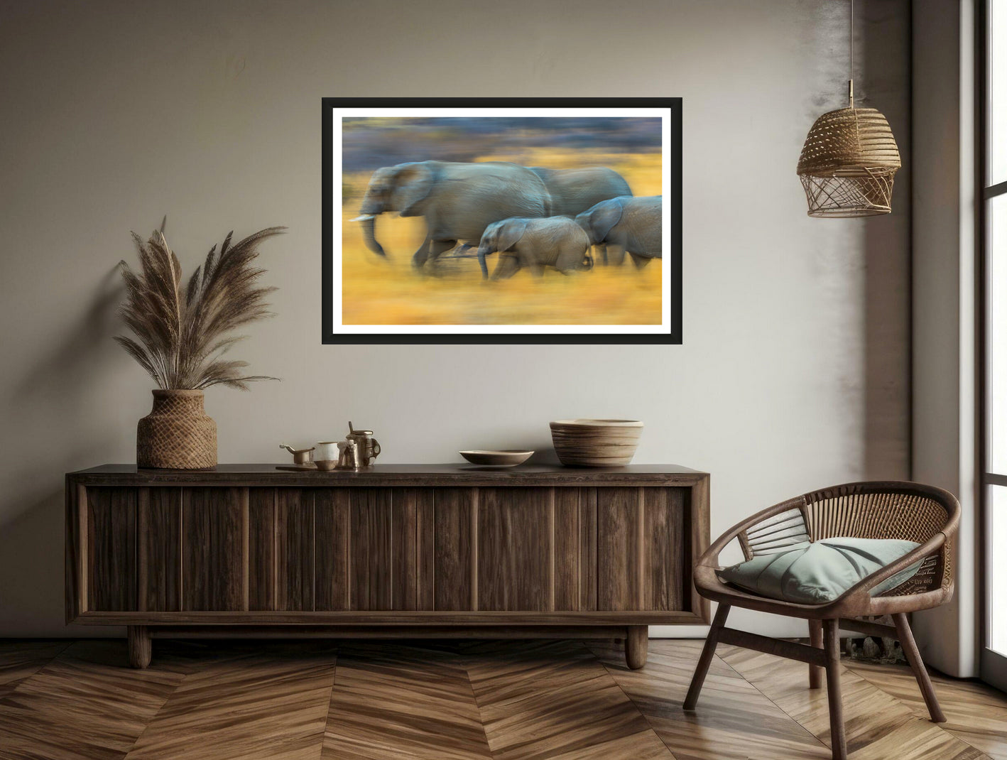 A motion blur photograph of a herd of African elephants marching through the dry yellow landscape hanging on a brown wall above a commode and a chair.