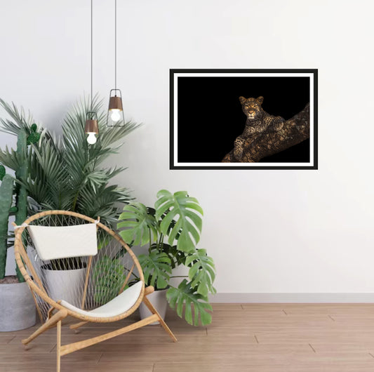 A photograph of a beautiful female leopard hanging over a huge Marula branch staring into the camera hanging on a white wall in a room with a chair and plants next to it.