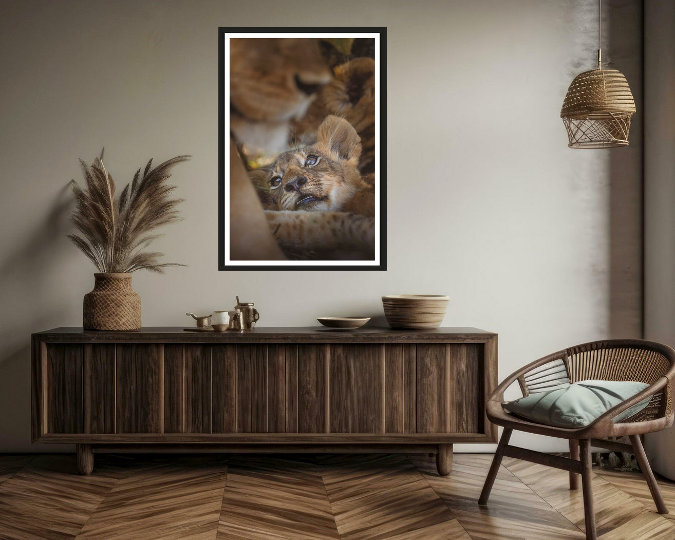 A photograph of a cute lion cub lying in the middle of the pride hanging above an elegant sideboard with deco and a chair.