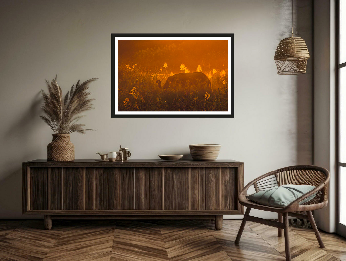 A photograph showing an elephant's silhouette standing in the reeds with an orange sky during sunset hanging on a brown wall above a commode with a chair. 